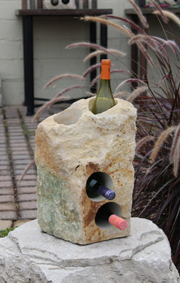 Rough textured Limestone Wine Rack with two vertical holes and two horizontal holes, showing 3 bottles of wine, all set atop a boulder pedestal.  17" tall