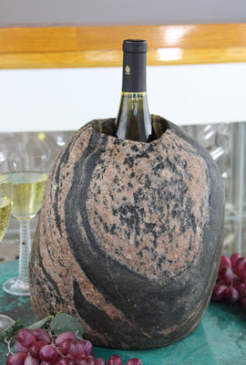 Oval shaped Granite stone wine chiller, 11" tall with one 3-1/2"  diameter hole 8" deep and holding one bottle of wine, set upon table with grapes and two glasses of white wine.