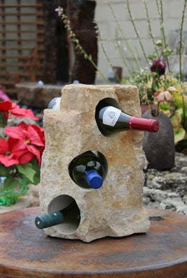 Light beige Limestone Wine Rack 14" tall, with three horizontal holes from top to bottom each offset from the next by 45 degrees, showing 3 bottles of wine, all set atop a small table.