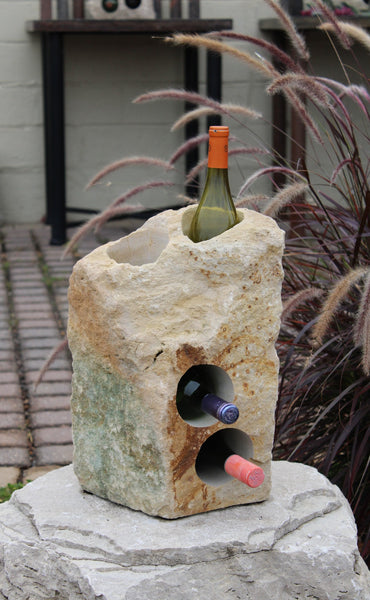 Rough textured Limestone Wine Rack with two vertical holes and two horizontal holes, showing 3 bottles of wine, all set atop a boulder pedestal.  17