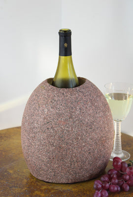 Oval Pink Granite Stone Wine Chiller 9" tall with one  large vertical hole, showing one bottle of wine, set atop small table with red grapes and a glass of white wine.